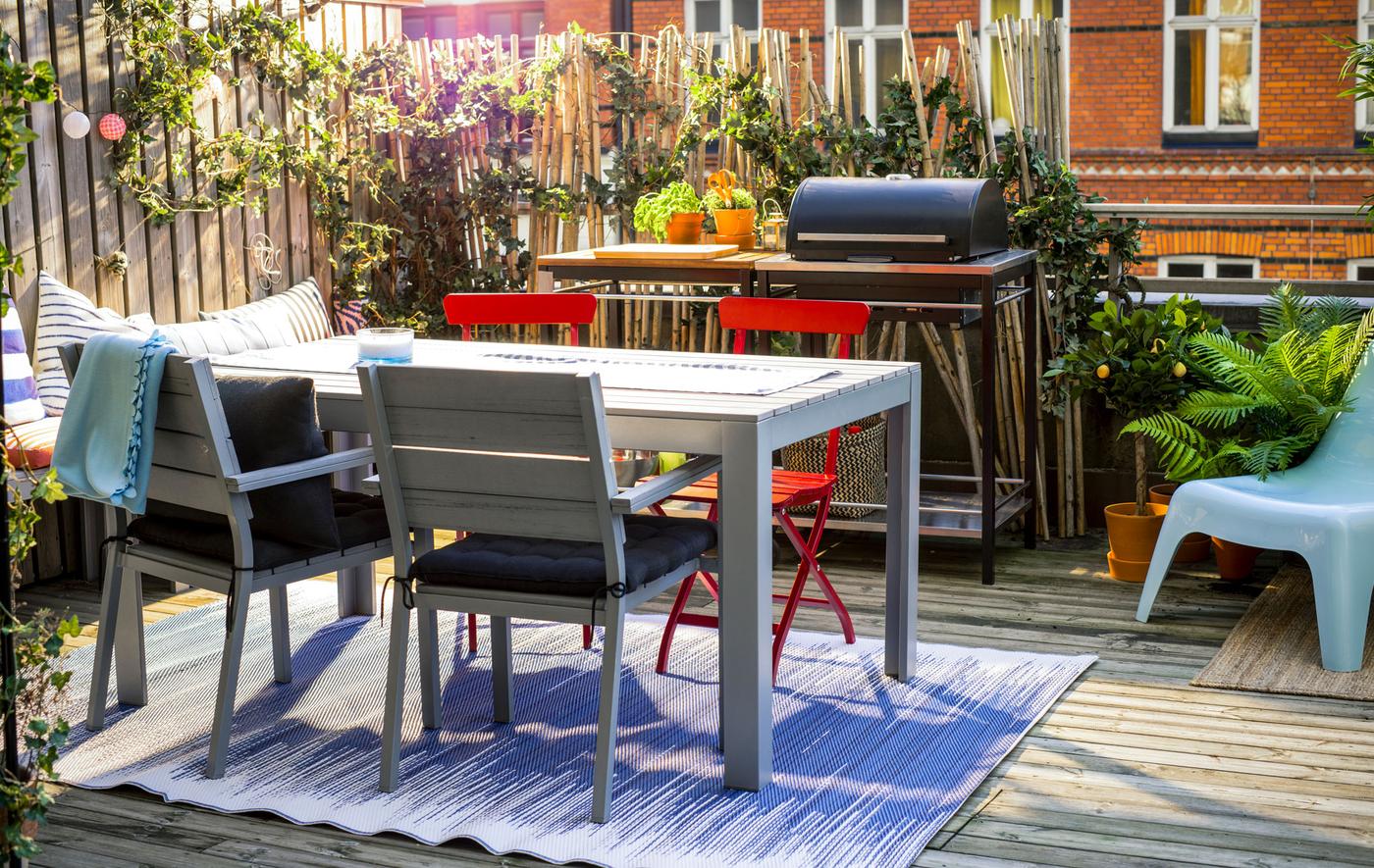  A shot of a balcony with a table and chairs, bench, grill and lots of plants.