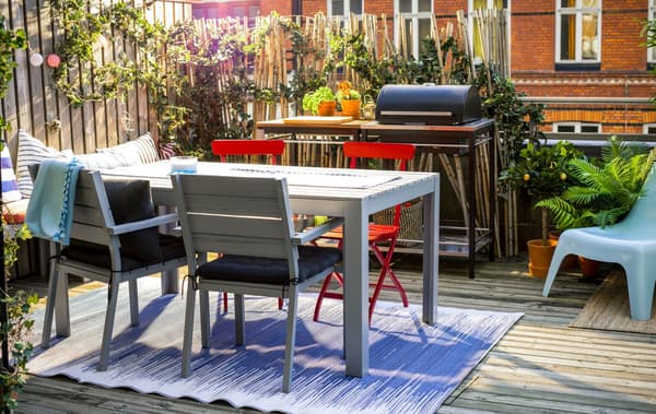 A shot of a balcony with a table and chairs, bench, grill and lots of plants..