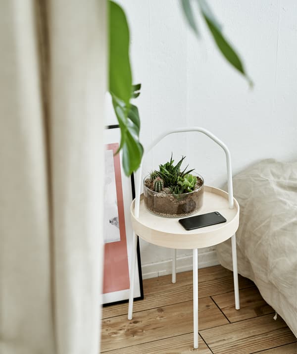 A side table with terrarium in a white bedroom.