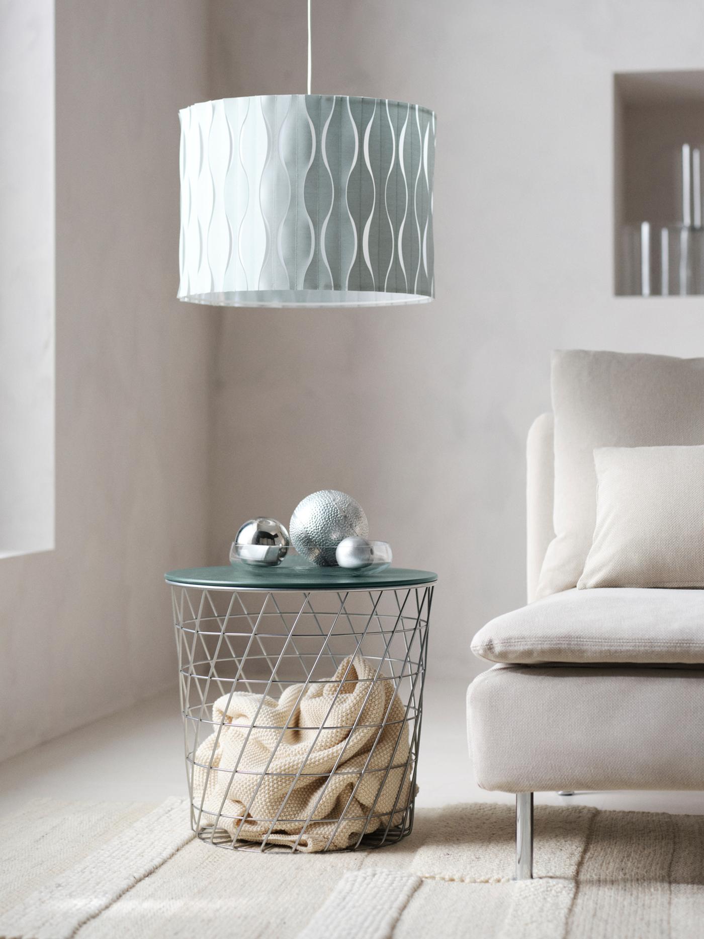 A silver and dark grey-green KVISTBRO storage table with a throw in it. And a LÖKNÄS lamp shade hanging from the ceiling.
