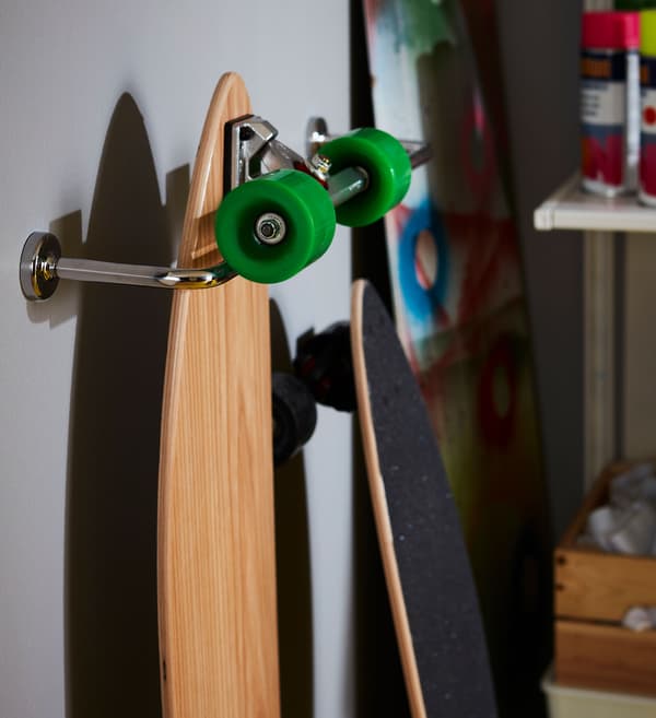 A skateboard hanging from a chrome effect IKEA VOXNAN towel rail attached to a wall.