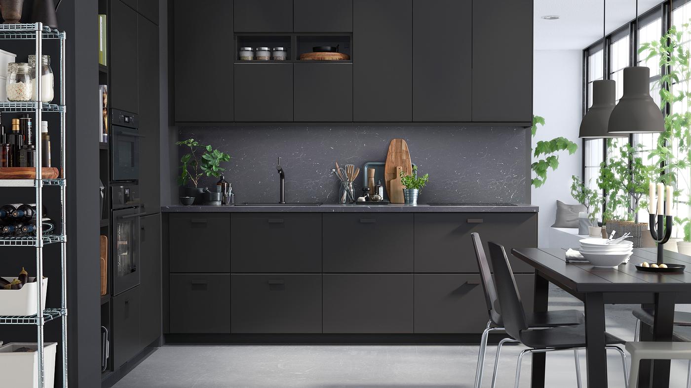 A sleek kitchen with anthracite units, dark grey walls and a black dining table and chairs.