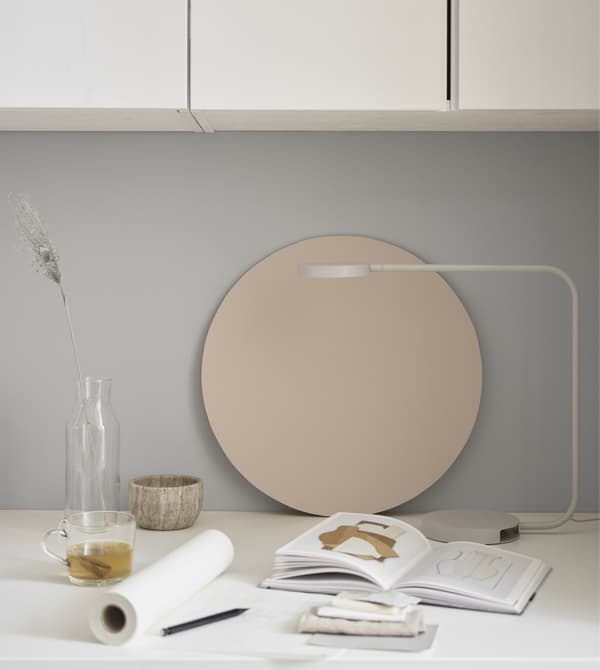 A slender white lamp at a desktop workspace with paper, notebook and a few decorative items.