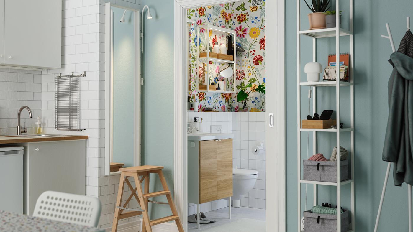 A sliding door opens up from the kitchen to a colourful bathroom with floral wallpaper and a small washstand.