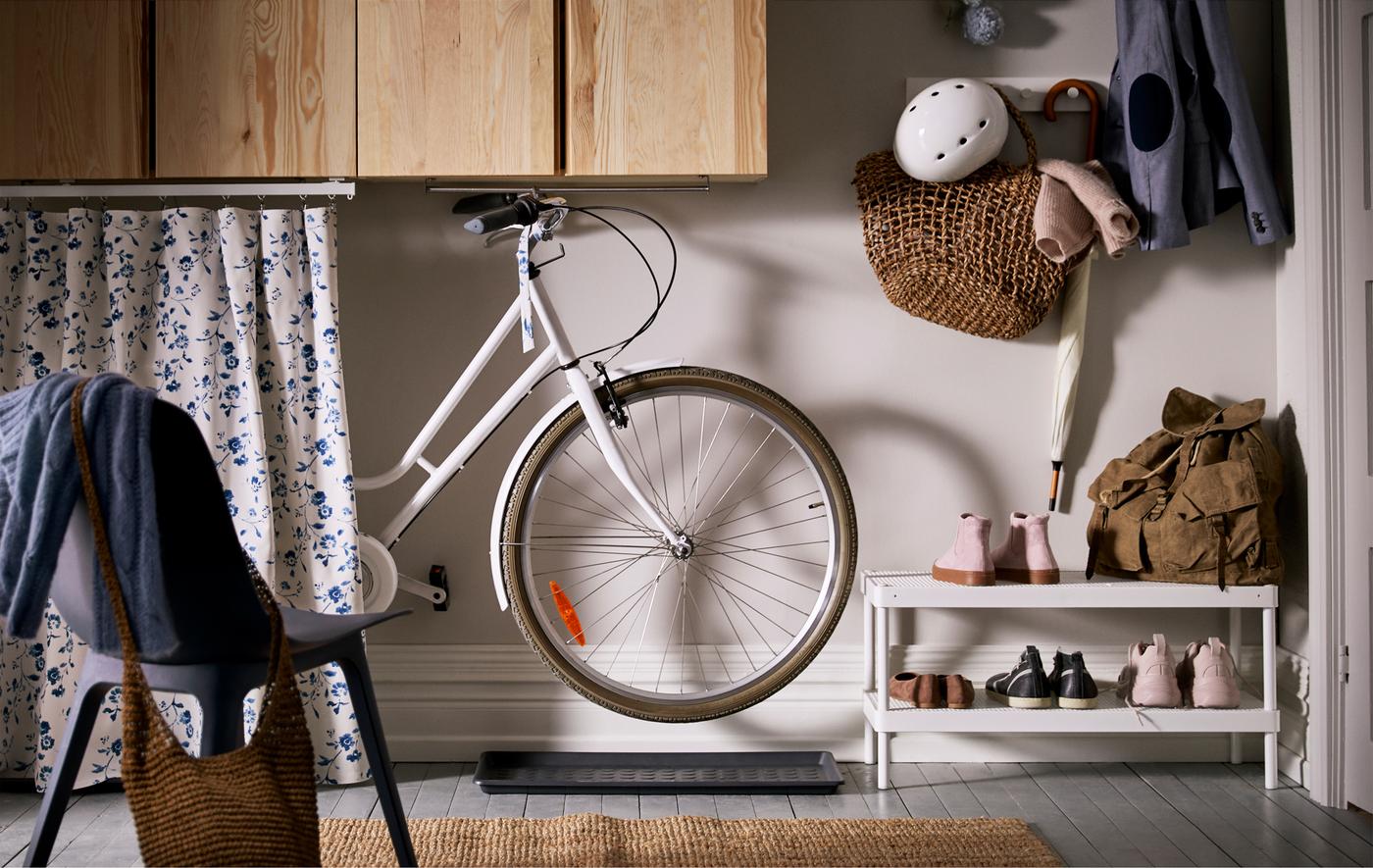 A sliding length of fabric hides a bike hung from a rail underneath wall cabinets in a hallway, shoe mats under the wheels.