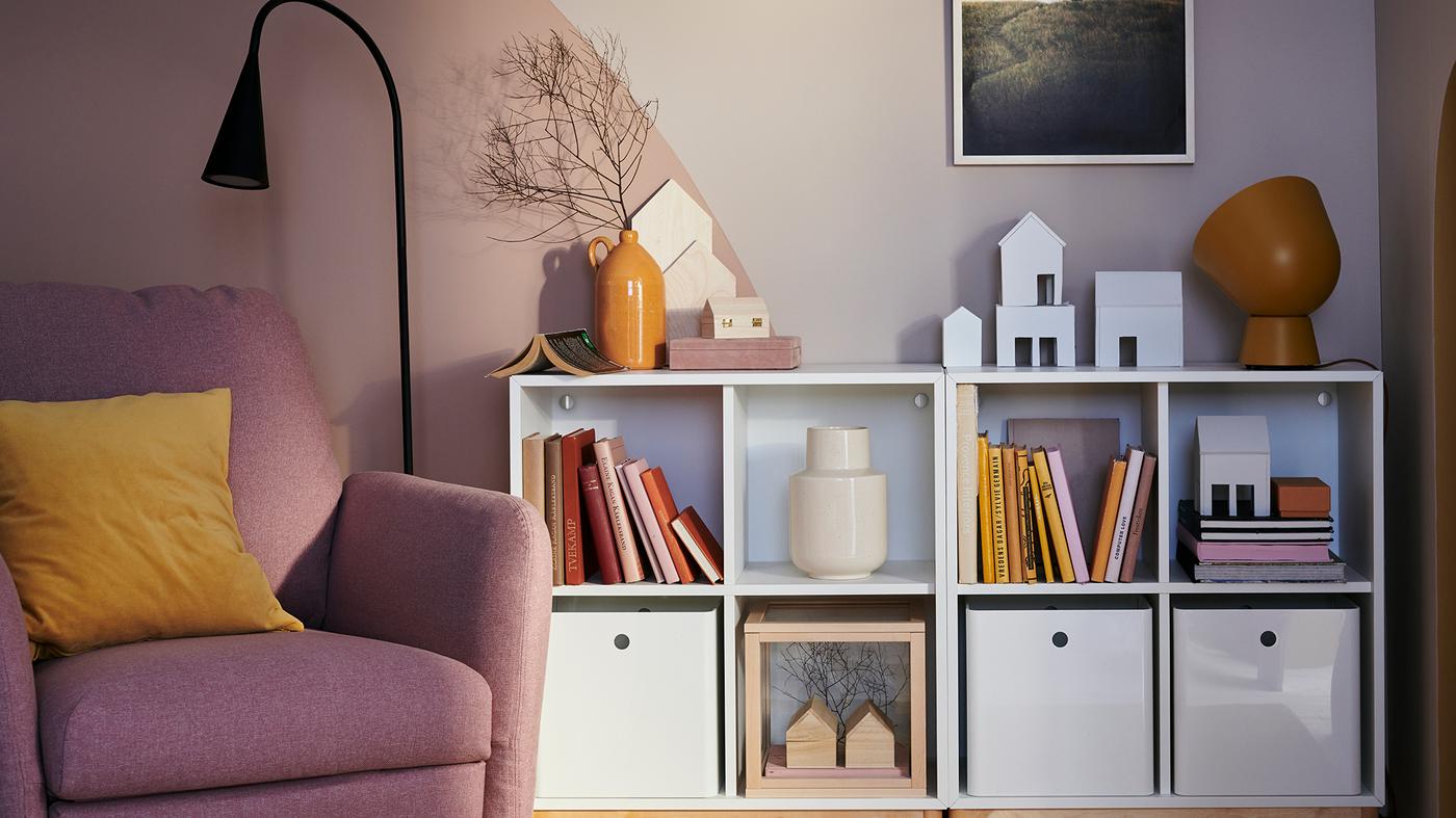A slightly messy living room with a blue sofa, a shoe rack, some stackable storage boxes and a half-full FRAKTA bag.