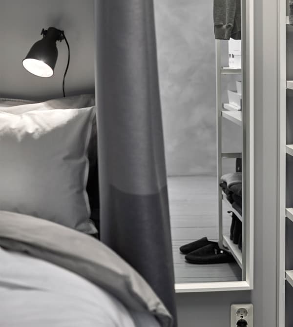 A small black reading lamp shining light down on the bed, mounted to the wall at the headboard of the bed.