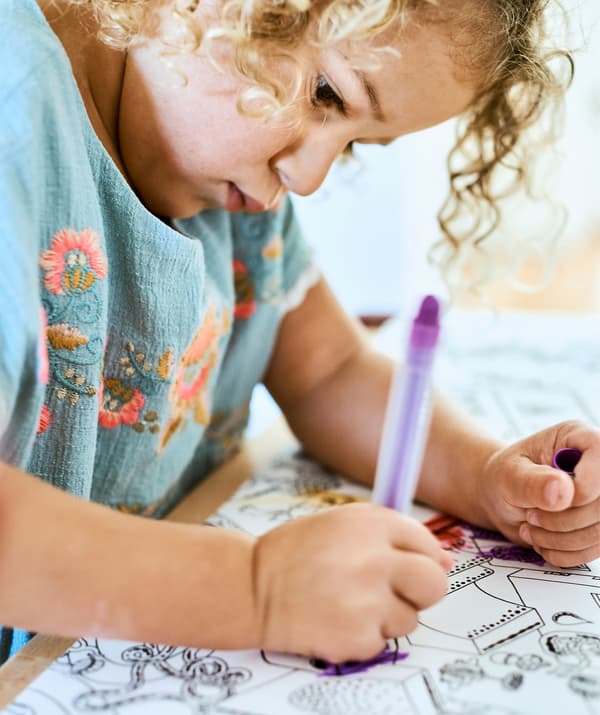 A small child coloring in an illustration with a purple crayon.