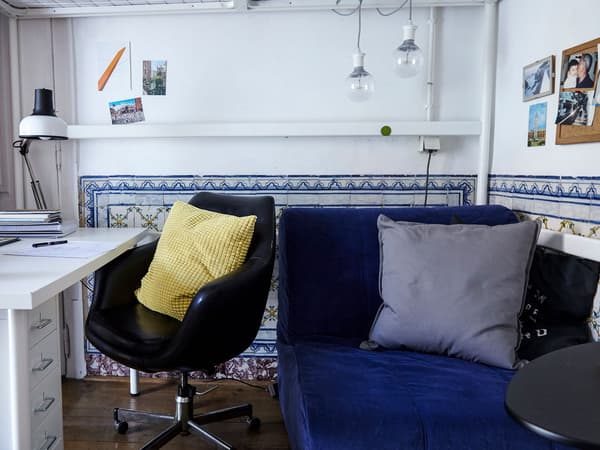 A small desk, black chair, and blue sofa bed create a space that’s also a second sleeping area in this bedroom.