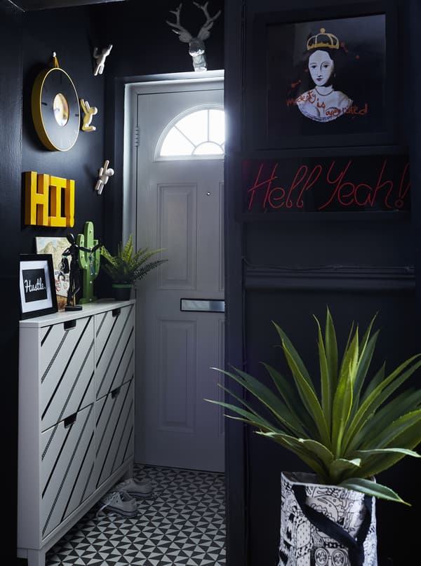 A small hallway with narrow shoe cabinets in white with black diagonal stripes, against black walls.