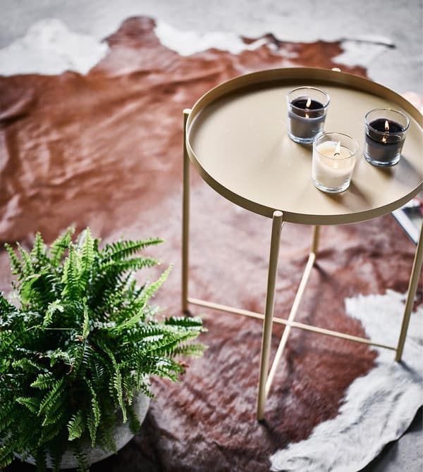 A small indoor fern next to a side table sitting on a cowhide rug.