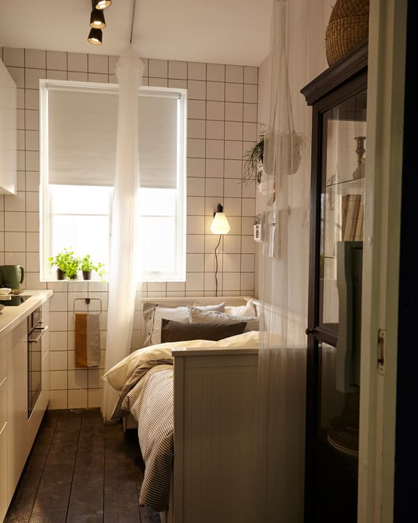 A small kitchen used as a temporary bedroom with the help of a sofa-bed and a curtain that acts as a room divider.