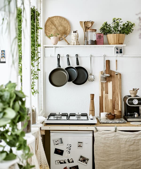 A small kitchen with hob, hanging utensils and a shelf for display.
