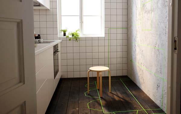  A small kitchen with one unfinished wall. Green tape marks the future placement of storage furniture, tables and chairs