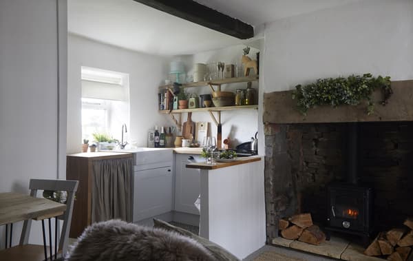 A small kitchen with open shelves above the worktop, next to a large fireplace.