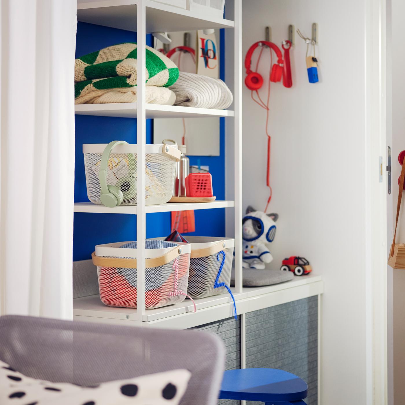 A small Scandi-style hallway has a white PLATSA open wardrobe with baskets and clothes on its shelves, against a blue wall.
