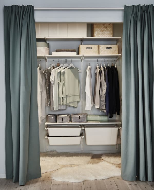 A small walk-in closet made of adjustable open ALGOT shelves, rails and drawers, finished off with some throw rugs.