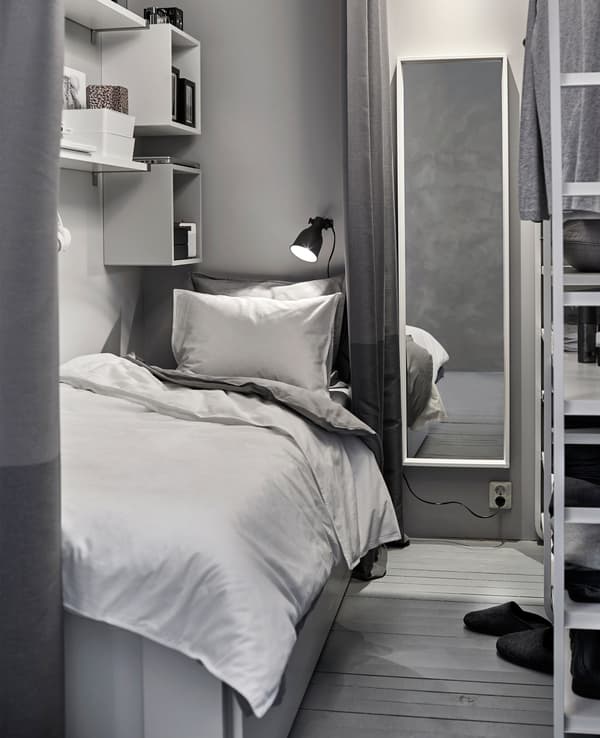 A small white and grey sleeping space is created in a shared space with a wardrobe.