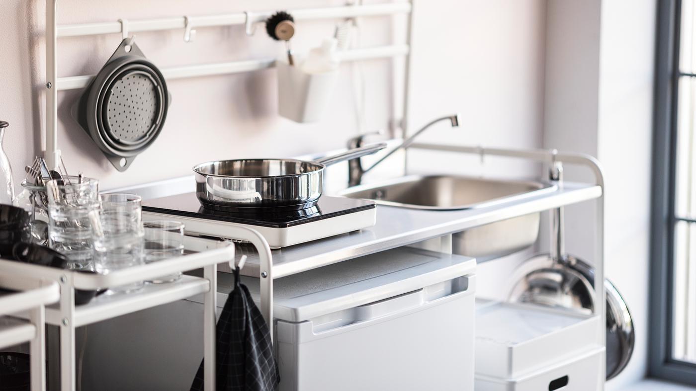 A small white mini kitchen with a portable induction hob and a small fridge.