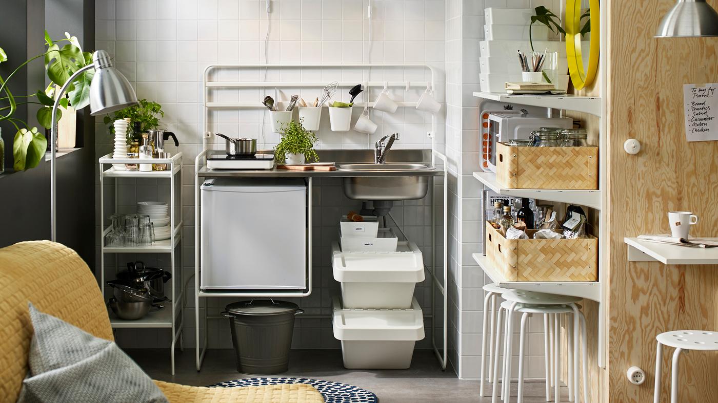 A small white mini-kitchen with a portable induction hob and a small fridge. A white trolley stores kitchen supplies.
