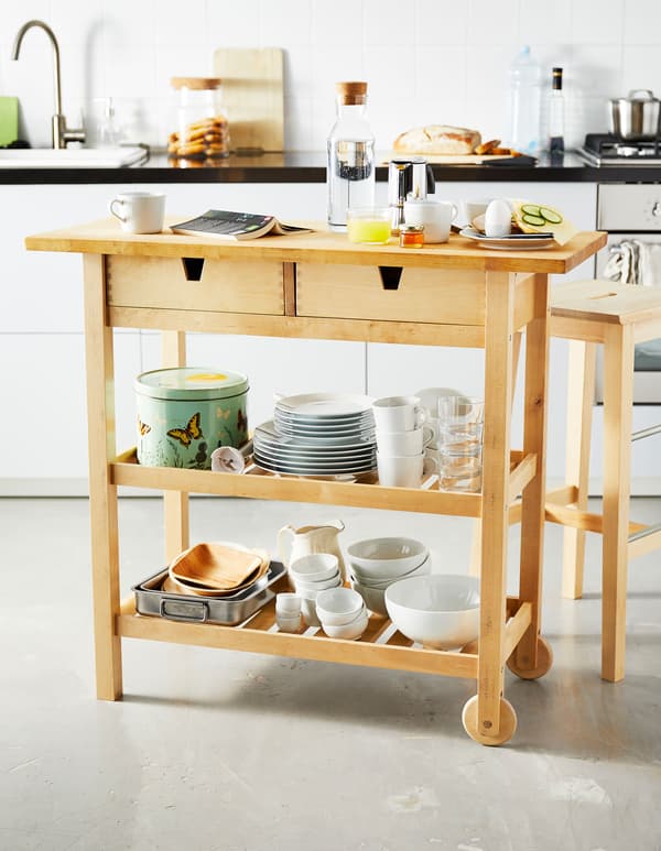 A small wooden kitchen island is set with breakfast foods and stores tableware on the shelves below.