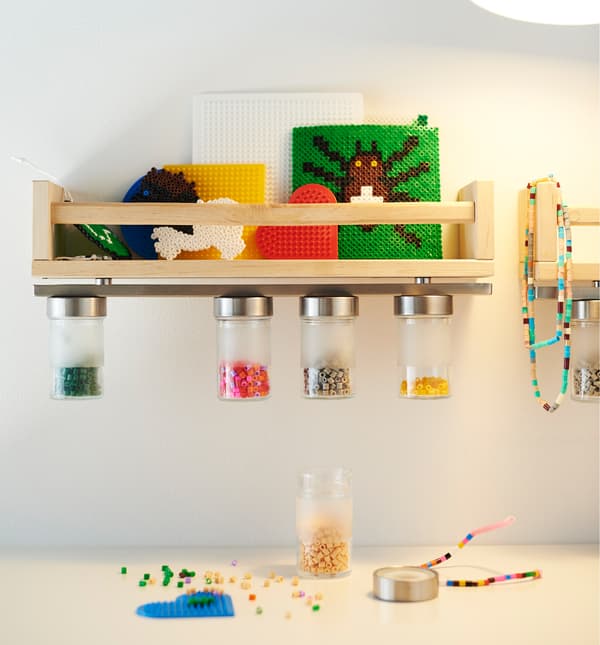 A small wooden shelf with a magnetic knife rack attached to the underside holds jars filled with beads.