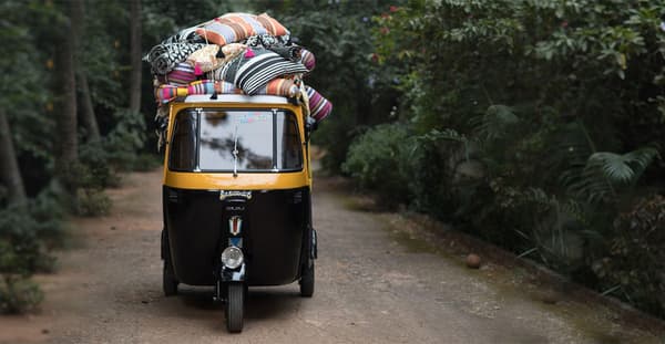 A small yellow and black coloured taxi in India carrying with colourful striped pillows on top.