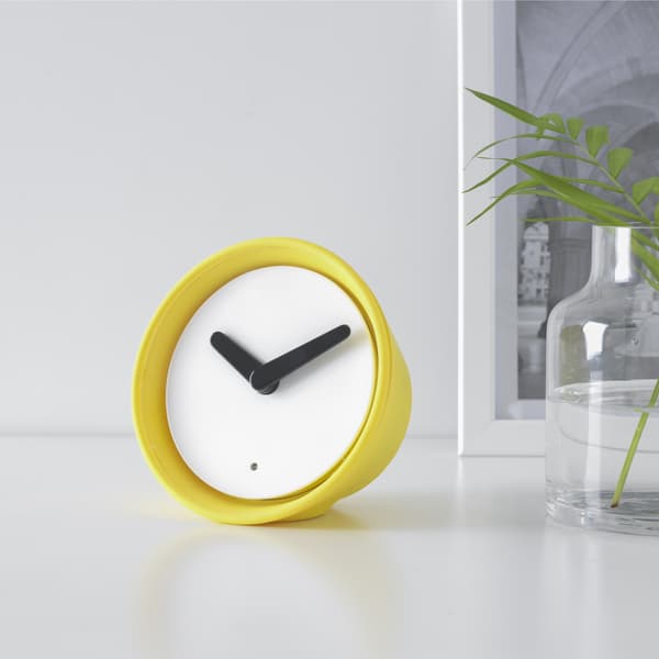 A small yellow table clock on a white surface.