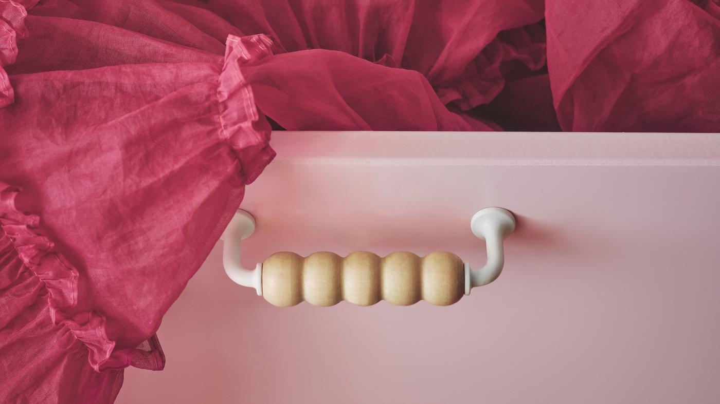 A SMÅSTAD drawer unit with a unique wooden handle placed on a light-pink drawer front with a cerise tulle skirt sticking out.