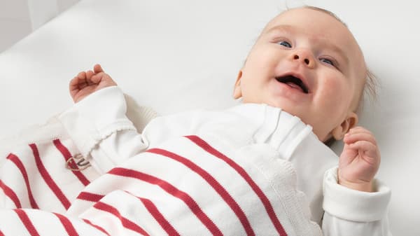 A smiling baby with a white and red striped RÖDHAKE blanket made from responsibly grown cotton.