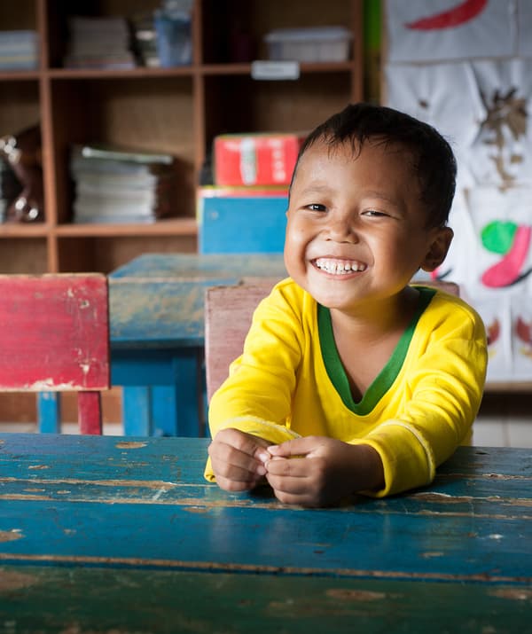 A smiling child sitting at a blue desk.