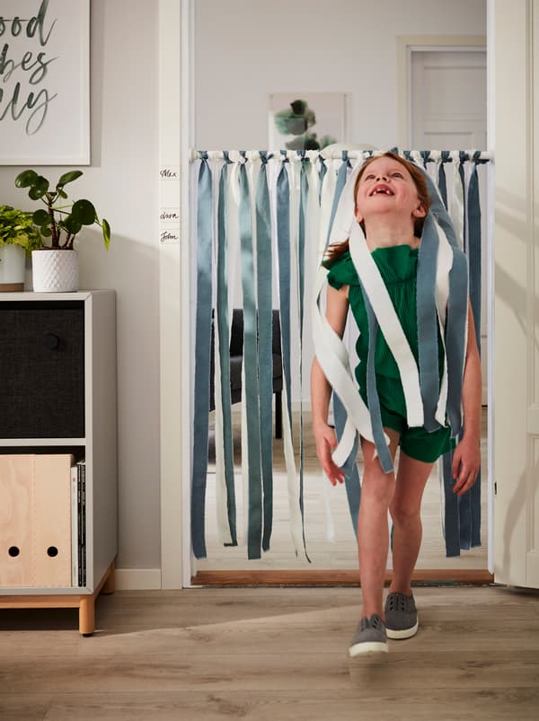 A smiling girl passes, head tilted back, under a BOTAREN rod decorated with strips of DITTE fabric and hung across a doorway.