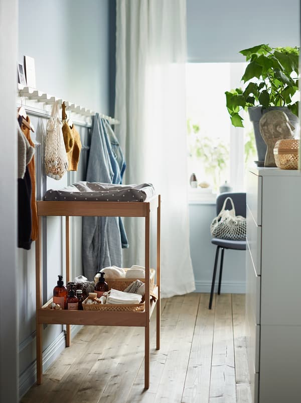 A SNIGLAR wooden changing table with a storage shelf and a long panel of white wooden hooks on the wall above it.