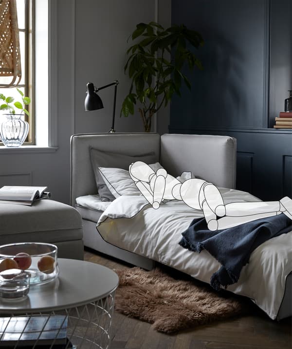 A sofa made for sleeping in a living room. The superimposed, sketched person lies on the side, a book on the side table.