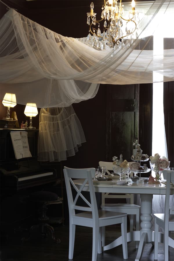 A softly lit theatrical chandelier and white dinner setting with table decorations.