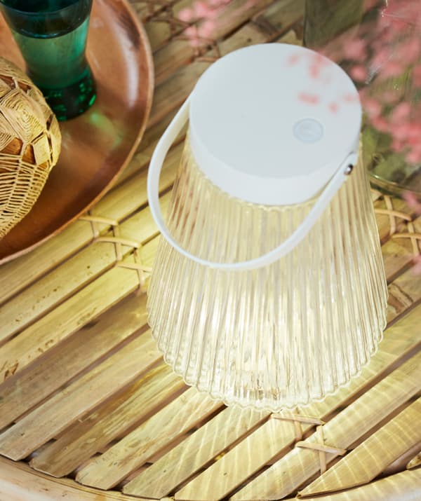 A solar-powered SOLVINDEN floor lamp stands next to tray on a tabletop made up of thin wooden slats, shedding a soft light.