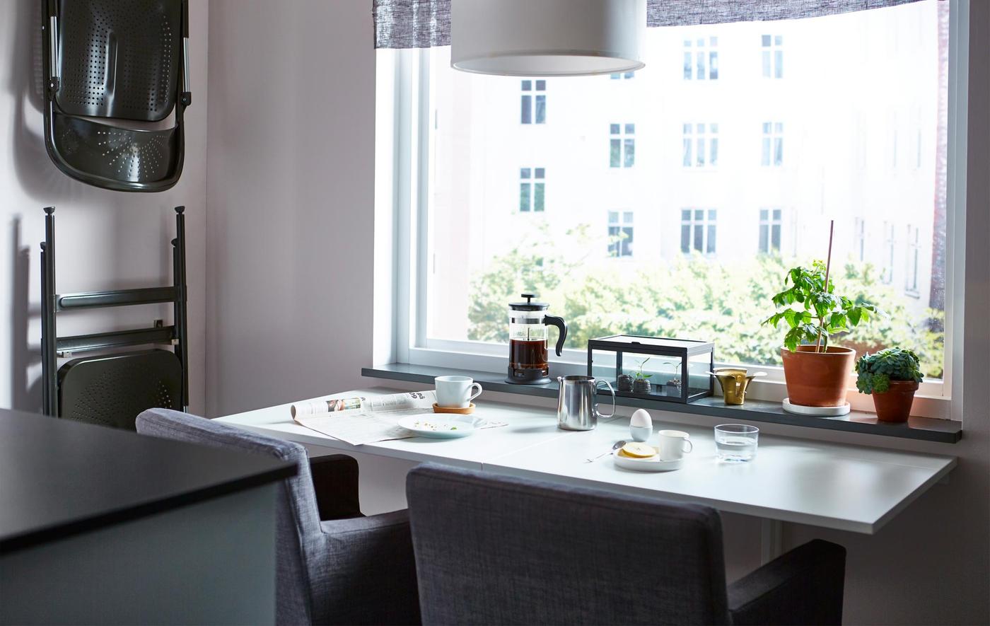 A space-saving dining table, prepared with breakfast, with two dining chairs facing a window.