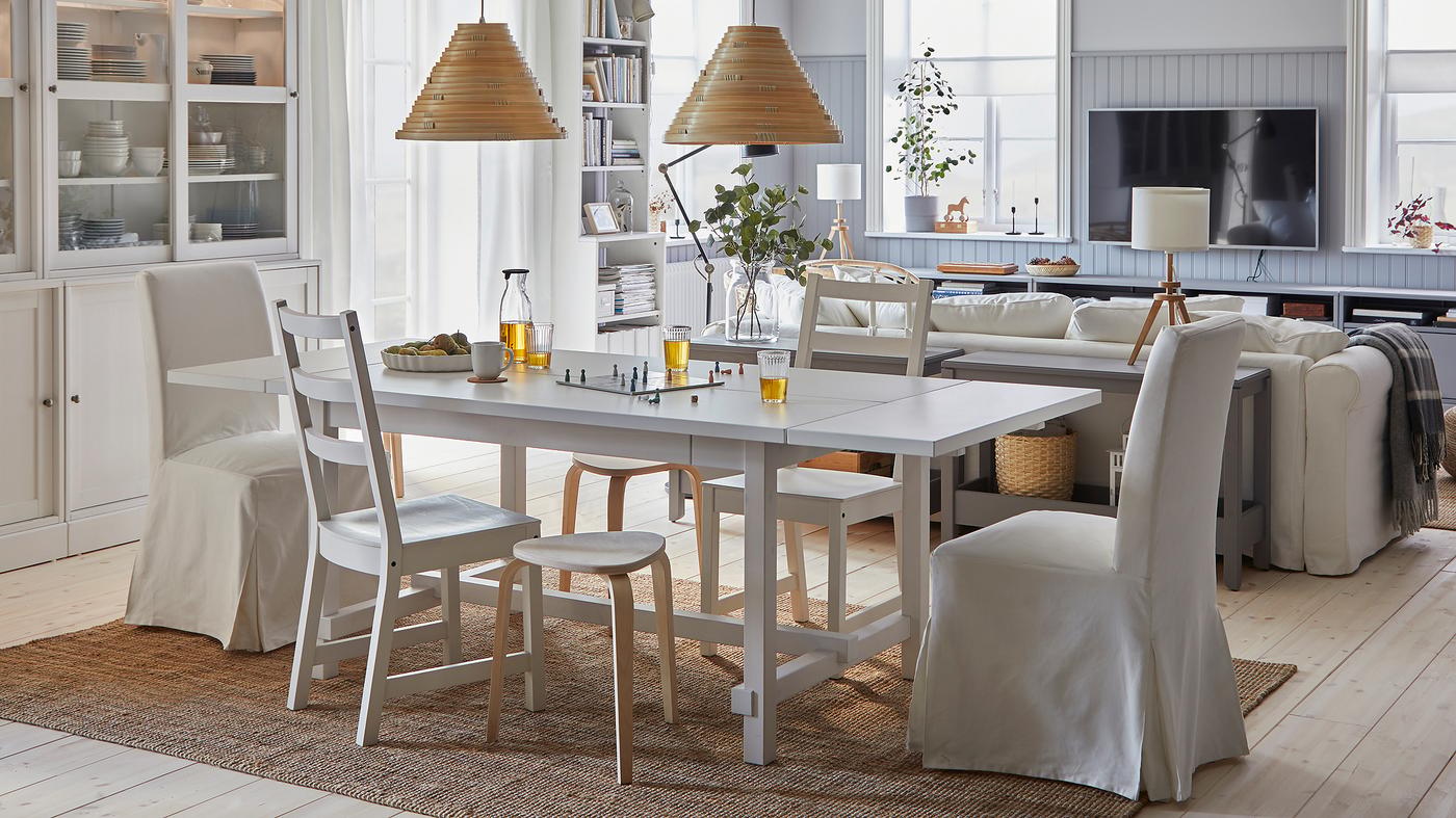 A spacious and bright dining room with a connected living room. The dining table is extended, and stools provide more seats.