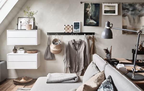 A spare room with a sloped ceiling is furnished with neutral coloured furniture, including a a sofa bed and a desk.