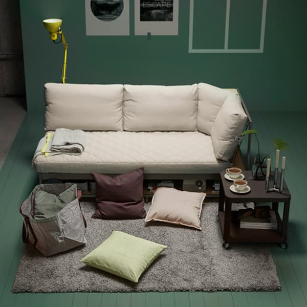 A staged living room scene with cream coloured sofa, cushions scattered on the floor and a side table.