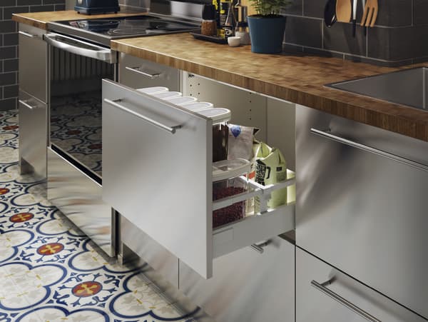 A stainless steel kitchen with a wood worktop in oak/veneer. One drawer is open, and lots of dry goods are stored inside.