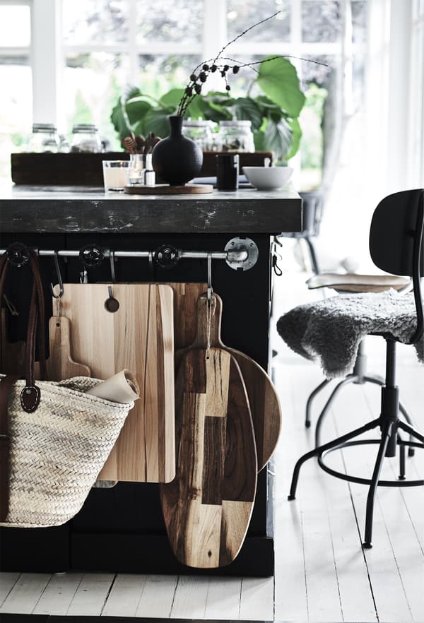 A stainless steel rail with different shaped wooden chopping boards, hanging at the back of a kitchen island.