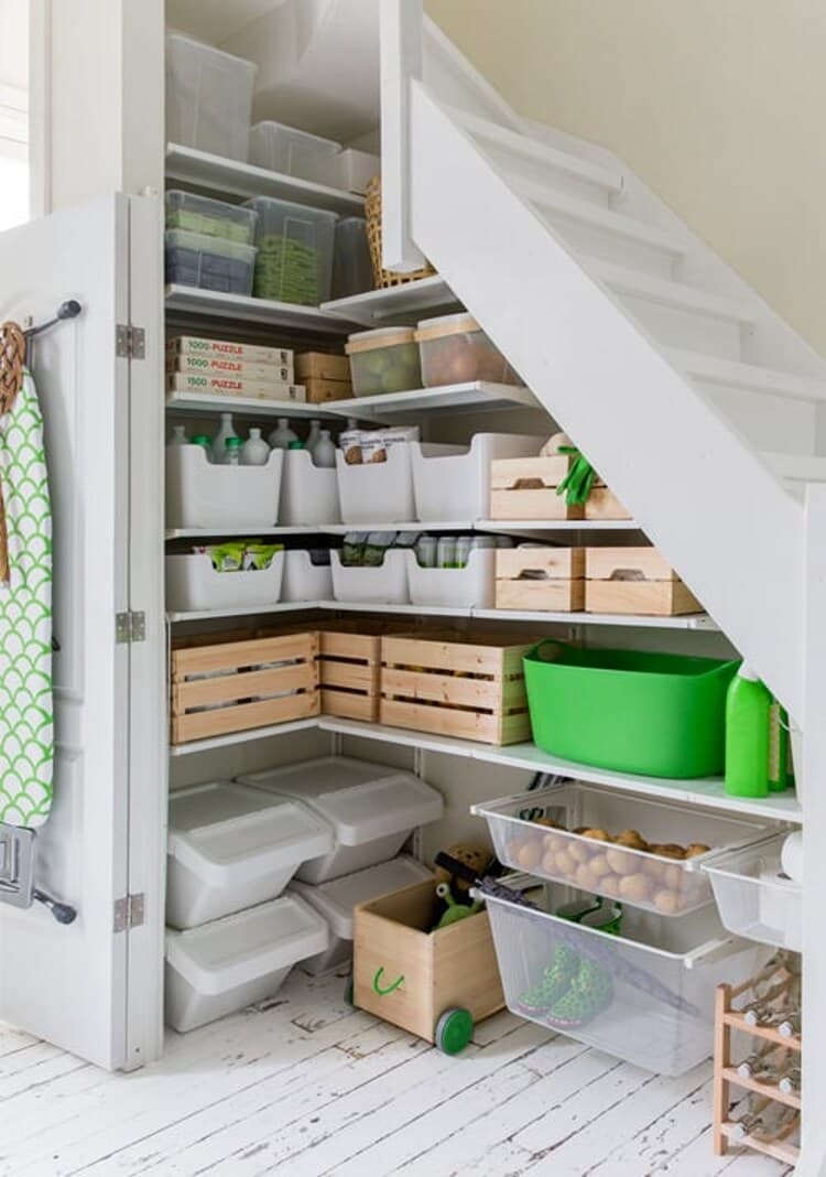 A stairs cupboard with wooden KNAGGLIG boxes and white storage bins containing various household items. On the floor is a JONAXEL storage combination.