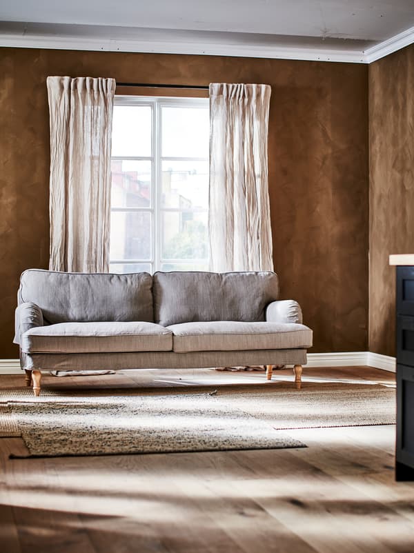 A STOCKSUND three-seat sofa in a brown room with French windows and accessories in natural textures.