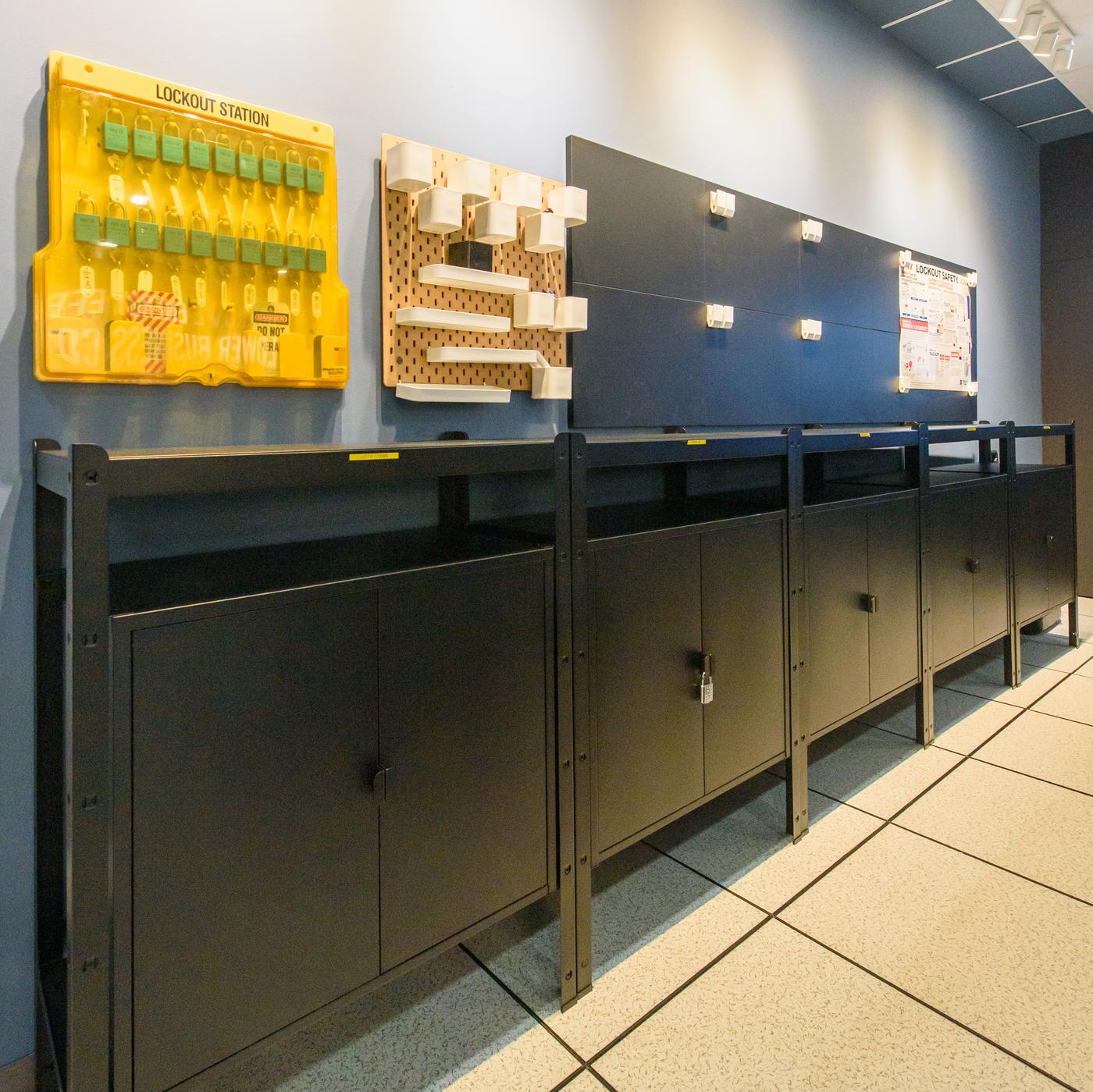 A storage area with black cabinets with pegboards on the wall on top.