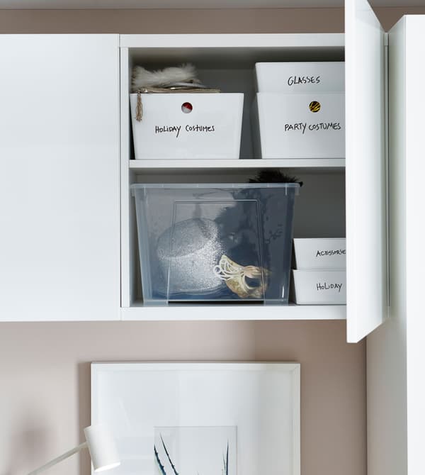 A storage cabinet above a bed is opened to reveal labeled storage boxes within.