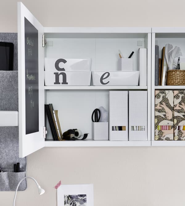 A storage cabinet above a desk is opened to reveal labeled storage boxes within.