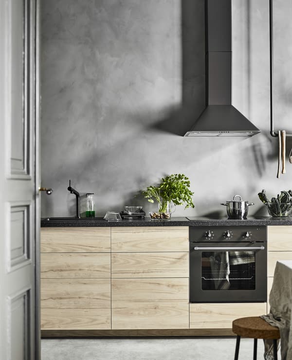 A straight-line kitchen with a row of base cabinets with ash fronts against a grey, concrete looking wall  