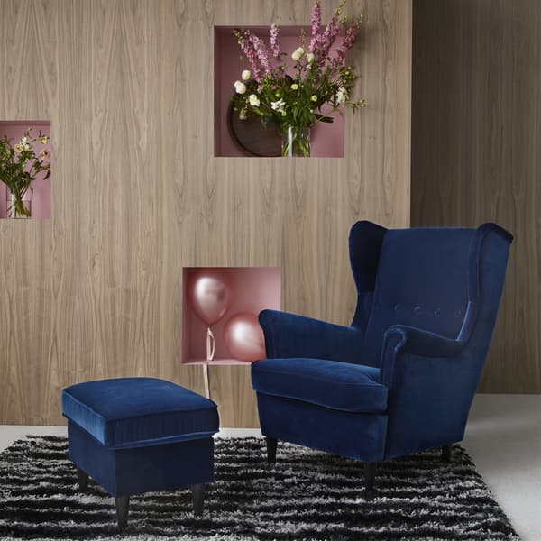 A STRANDMON wing chair in blue velvet with footstool on a black and white rug.