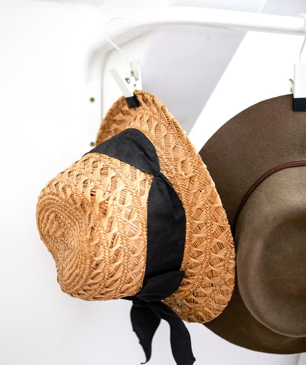A straw hat hanging on a hook on a rail on a white wall.
